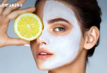 სახის ნიღაბი ციტრუსისგან Woman with a white facial mask holding a lemon slice over her eye during a skincare routine.