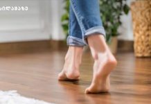 ფეხების მასაჟი – ბებიების მეთოდი Person walking barefoot on a wooden indoor floor, jeans cuffs rolled up at the ankle.